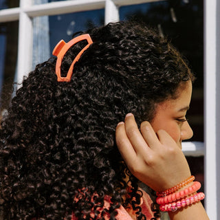 Person with curly hair wearing an orange hair clip 