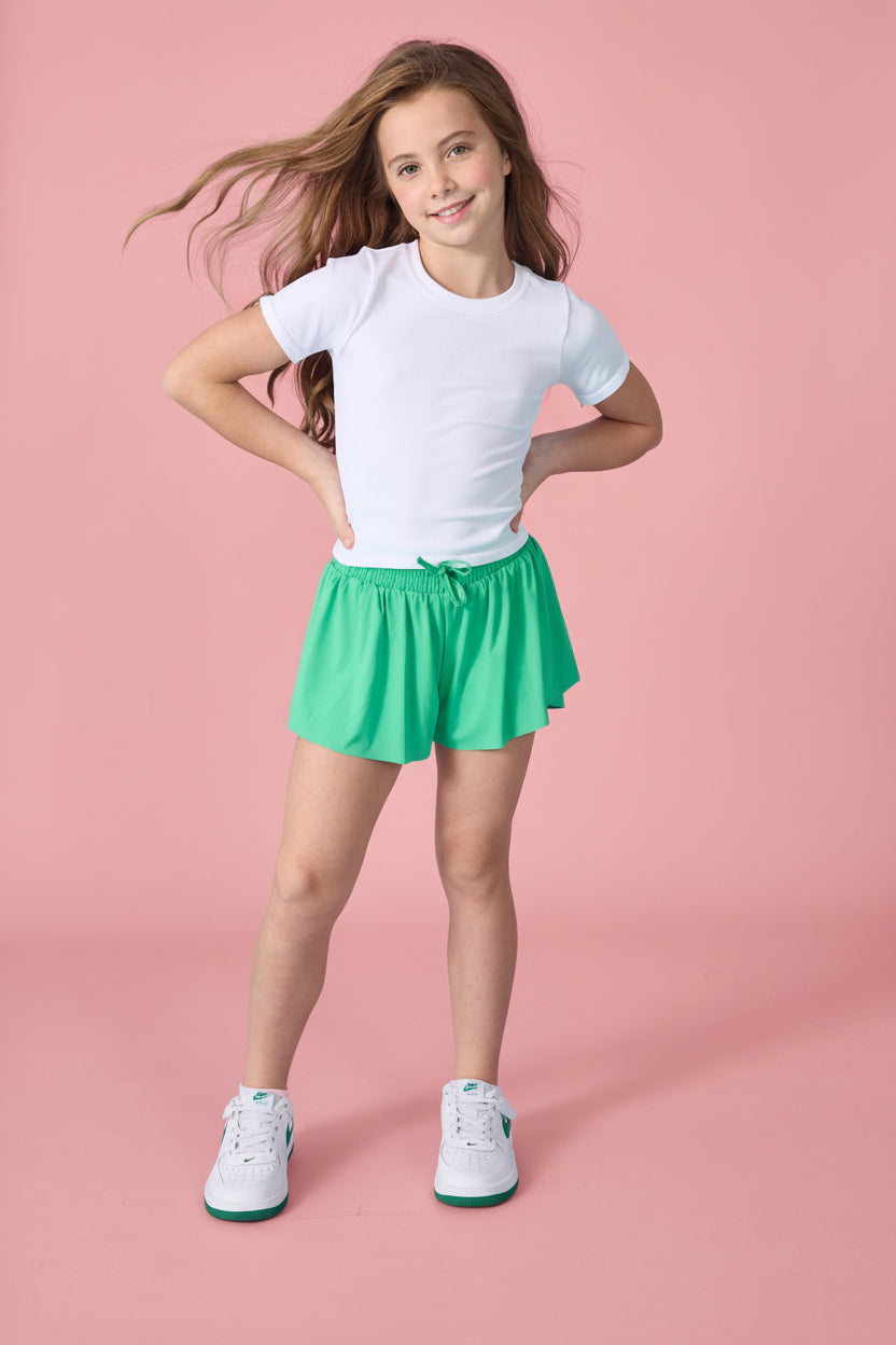 Young girl wearing a white t-shirt and green shorts on a pink background