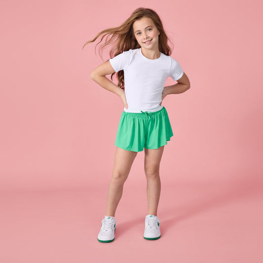 Young girl wearing a white t-shirt and green shorts on a pink background