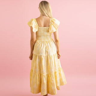 Woman wearing a yellow dress with ruffled sleeves on a pink background