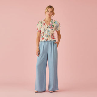 Woman wearing a floral blouse and light blue pants on a pink background