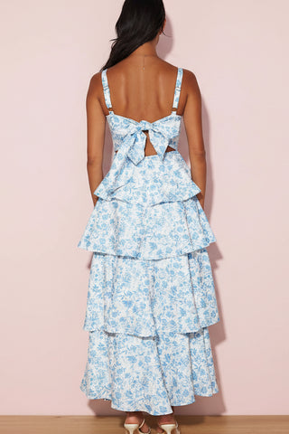 Woman wearing a blue floral dress with tiered layers on a pink background